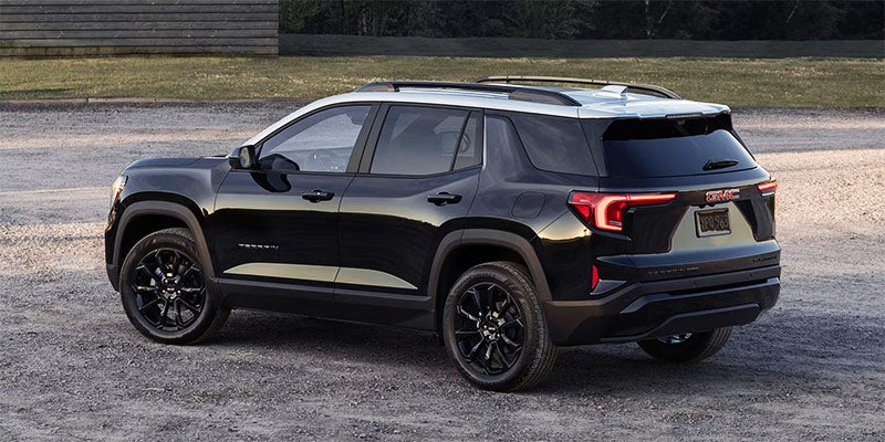 Black GMC Terrain SUV with a white roof and black wheels, parked on gravel, viewed from the rear passenger side.