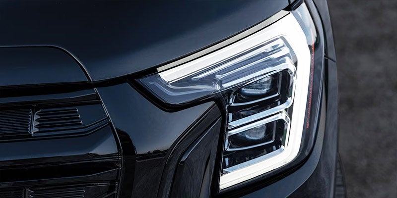 Close-up of a modern vehicle's angular LED headlight and part of a dark grille, both illuminated.