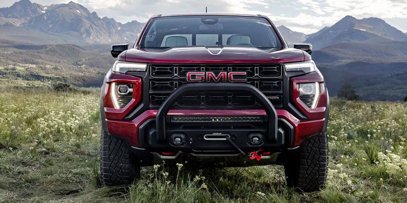 Front view of a GMC pickup truck with a bull bar, light bar, and winch, in a mountainous, grassy landscape.