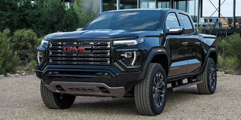 Black GMC Denali pickup truck with red logo on grille, parked on gravel.