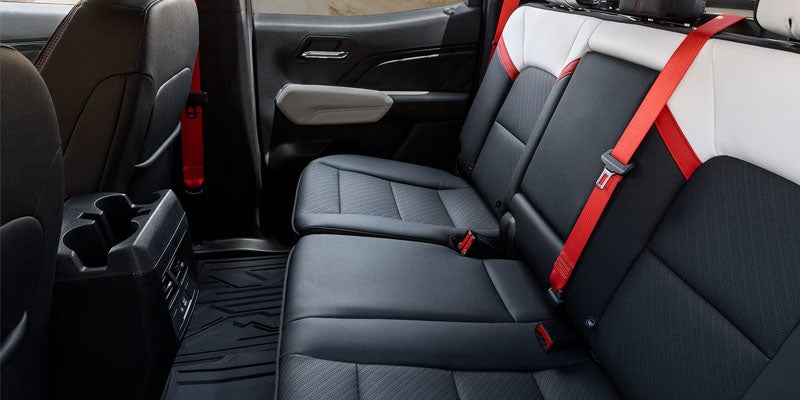 Rear interior of a vehicle with black and white seats, bright red seatbelts, and a console with cup holders.