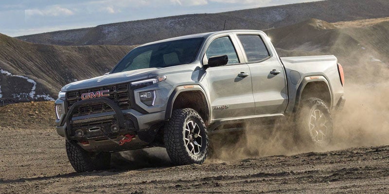 Light grey GMC Canyon AT4X pickup truck kicking up dust on rugged off-road terrain.