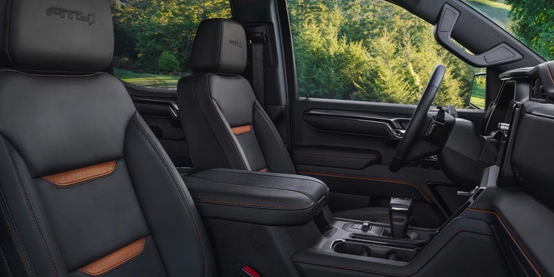 Black leather truck interior with orange accents, dashboard, steering wheel, and green trees outside the window.