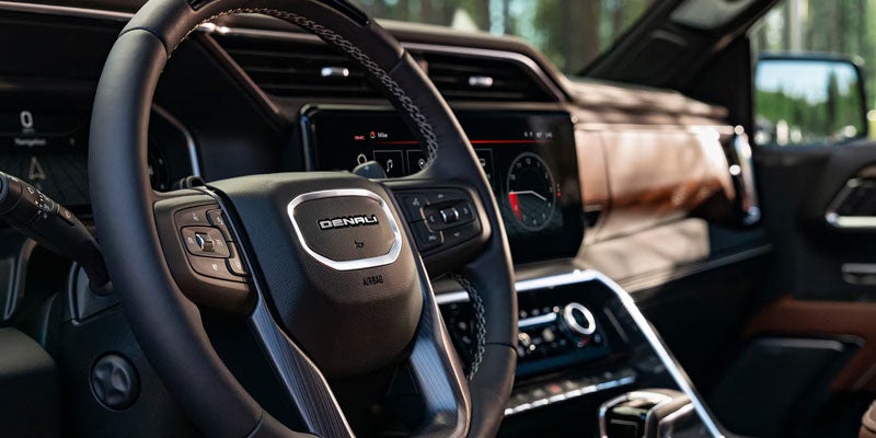 Car interior with a black leather "DENALI" steering wheel, digital dashboard display, and brown woodgrain trim.