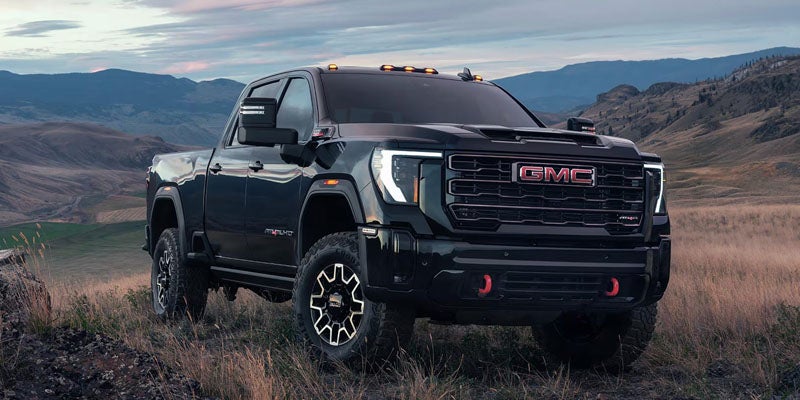 Black GMC pickup truck with red tow hooks, parked on a grassy hill overlooking a mountainous valley at dusk.