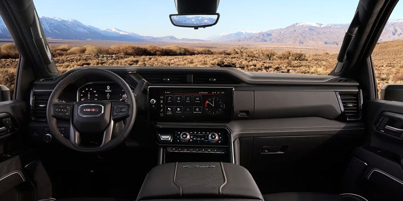 Modern dark truck interior with dashboard, infotainment screen, and steering wheel, overlooking a desert landscape with mountains.