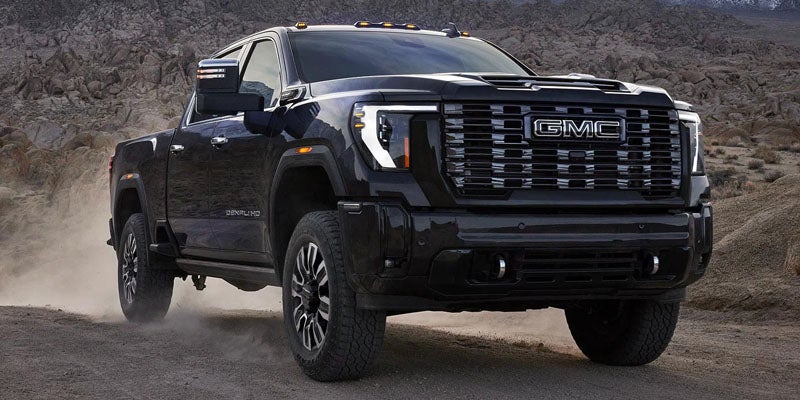 Black GMC Sierra truck driving on a dirt road, viewed from the front.