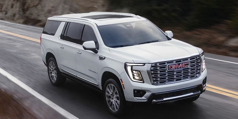 White GMC Yukon SUV driving on a paved road, with its front and right side visible.