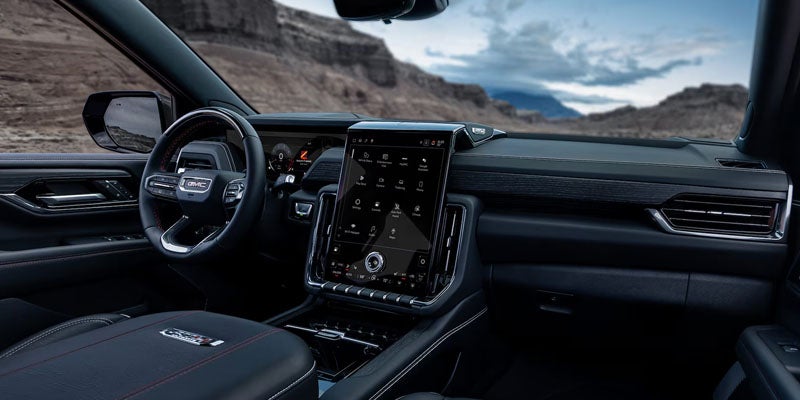 Car interior with a large central touchscreen, steering wheel, and desert mountains visible through the windshield.