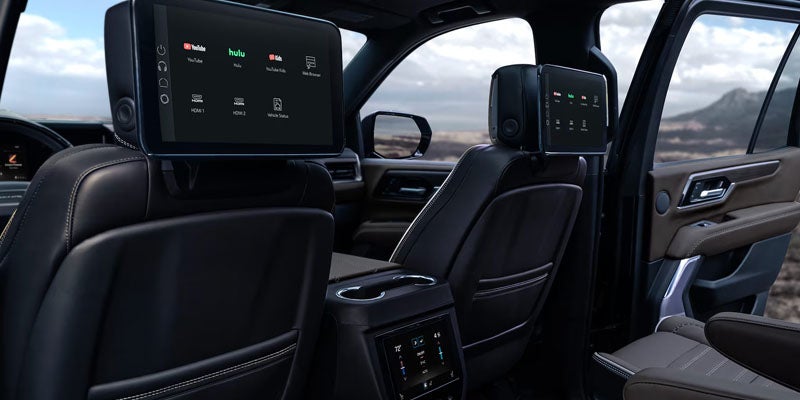 Car interior showing two rear-seat entertainment screens with app icons on the back of the front seats.
