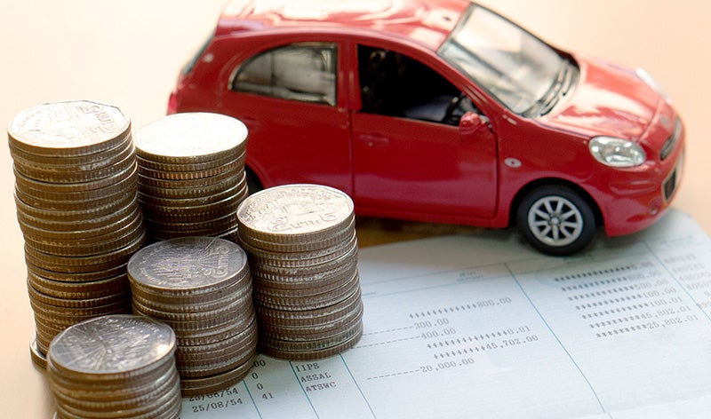 A red toy car sits next to stacks of coins on top of a printed document with numerical data.
