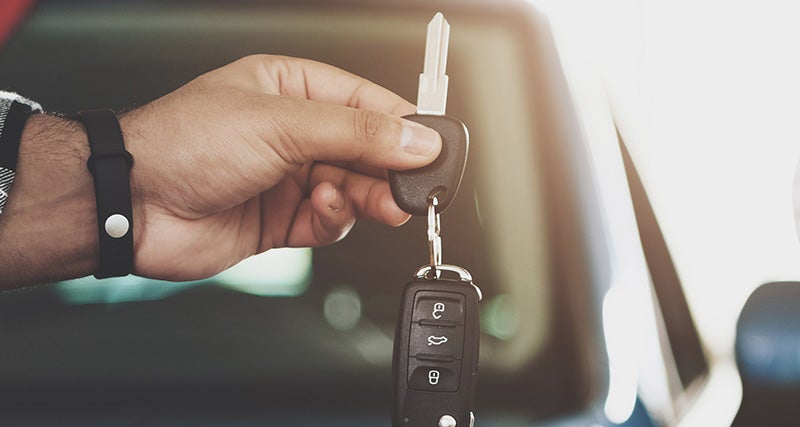 A person holds a car key with a black wristband, against a blurred car background.