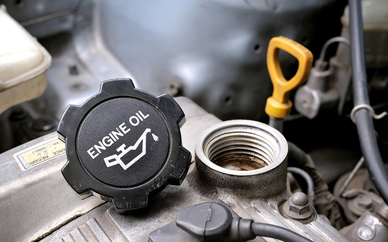 An engine oil cap with the words 'Engine Oil' printed on it sits atop a car engine.