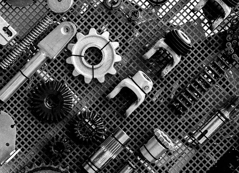 Various mechanical parts, including gears, springs, and cylinders, are arranged on a metal grid.