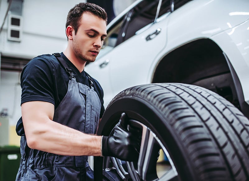 A mechanic wearing gloves adjusts a car tire while working on a vehicle in a garage.